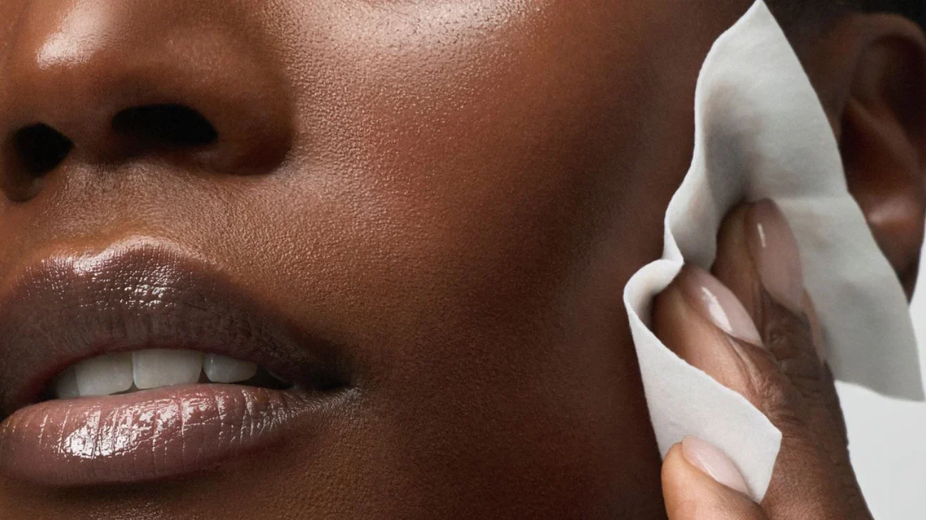 Close-up of a woman wiping her cheek with a cotton pad.
