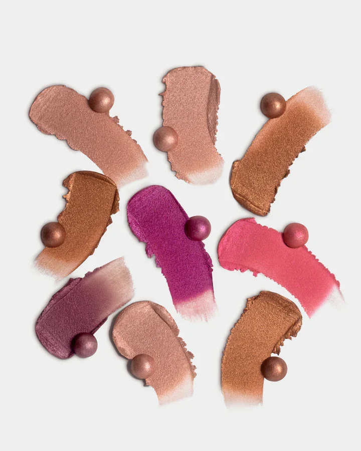Smeared swatches of bronze, berry and pink makeup with small pearls on a pale grey surface.