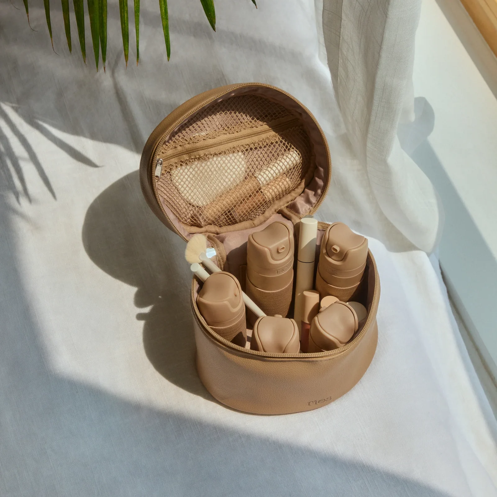 Tan travel case filled with matching refill bottles, sitting on white linen in sunlight.
