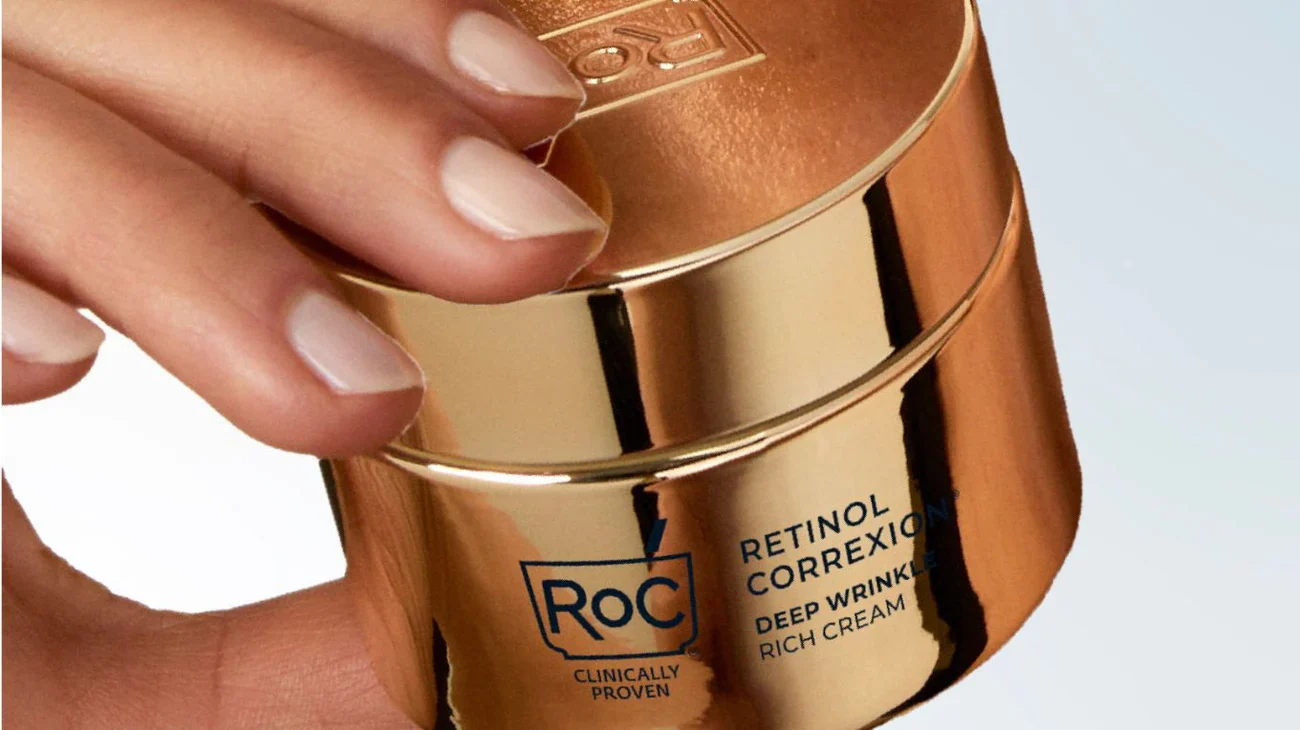 Fingertips opening a gold retinol jar.