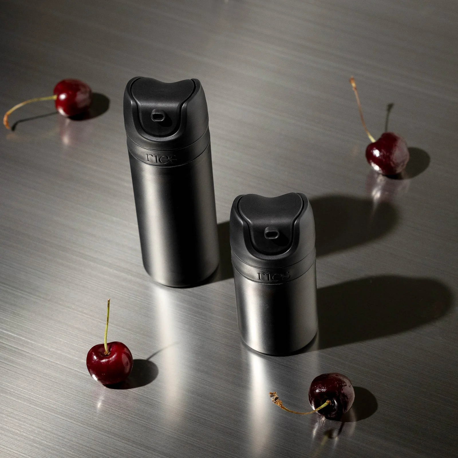 Matte black refillable bottles clustered with cherries.