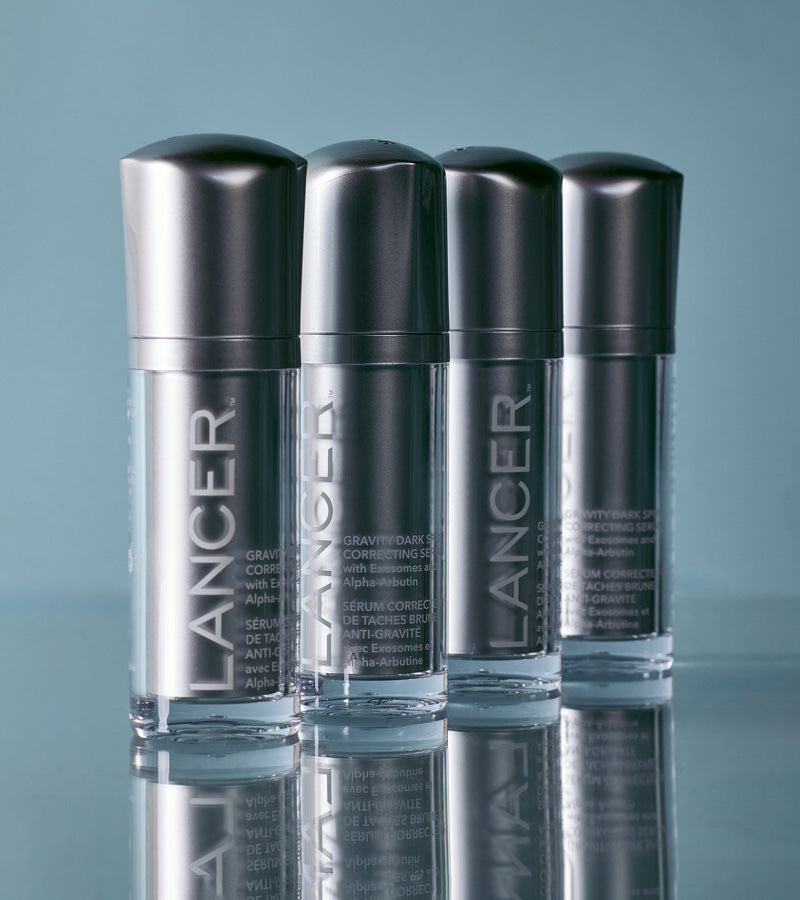 Four silver Lancer serum bottles reflected on a blue-grey surface.